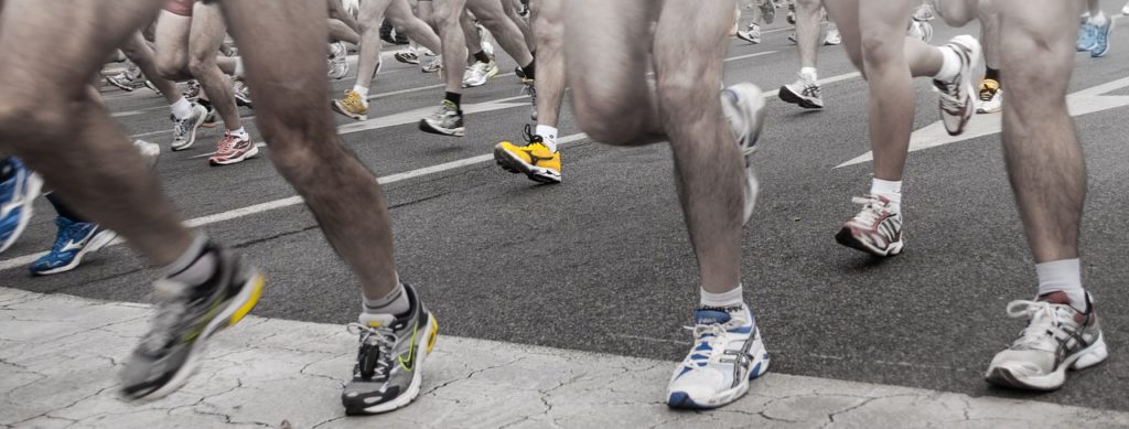Writing Half Marathon Plans - Racers running across a marker on the road, feet and colorful shoes