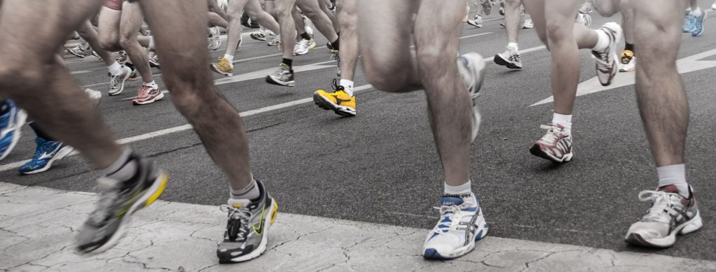 Half Marathon Pacing Strategy - Racers running across a marker on the road, feet and colorful shoes